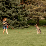 A short redheaded woman is pictured using a red Heather's Heroes long line with a large husky mix dog at the other end